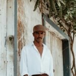 Fashionable man in classic attire posing by rustic wooden doors with a vintage feel.