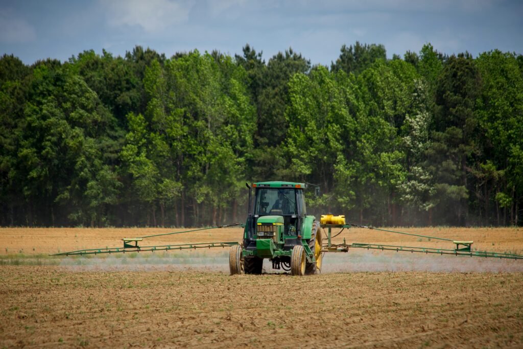 Tractor spraying fields with pesticides on a countryside farm in summer with a forest backdrop.